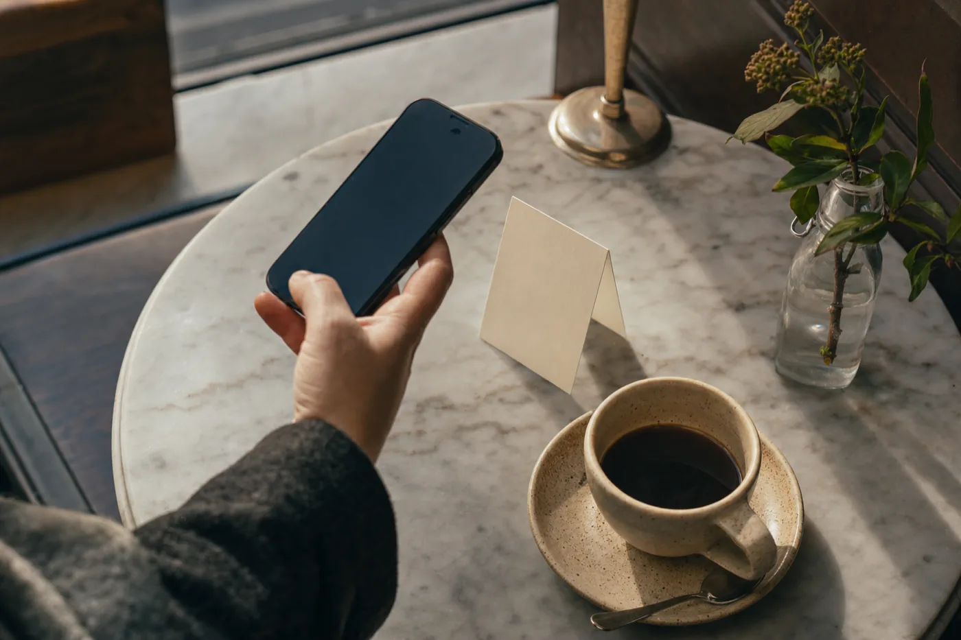 Hand med telefon över ett bordsställ på ett cafébord